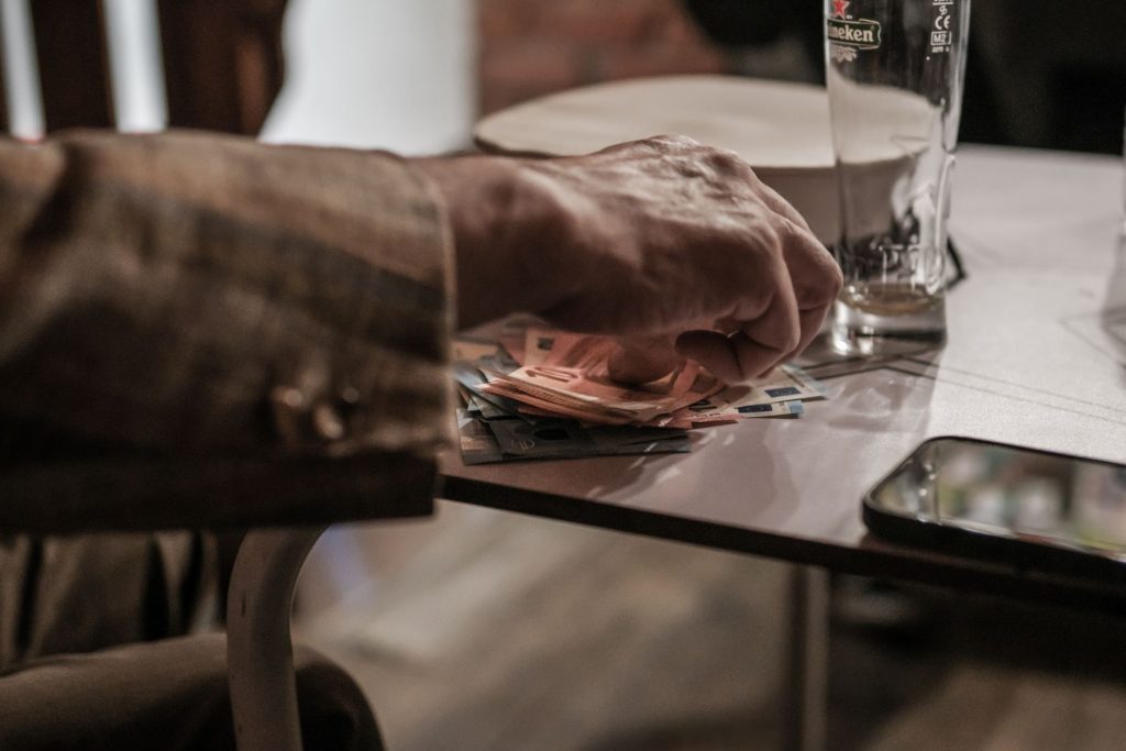 Dłoń licząca banknoty euro obok telefonu i pustej szklanki